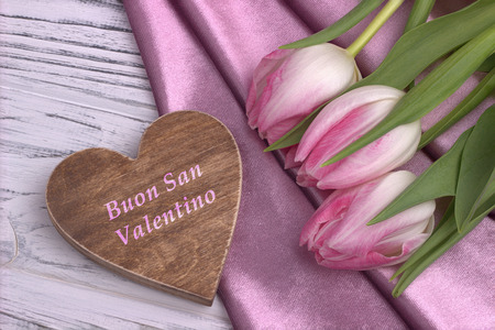 Valentine's day elegant still life with tulip flowers rose shine fabric rose and heart shape sign on white wooden background and lettering Happy Valentines Day in Italian. Loveの写真素材