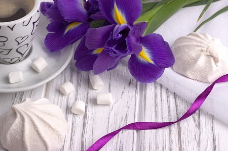 Still life with cup of coffe marshmallow zephyr iris flowers purple ribbon on white wooden background.の写真素材