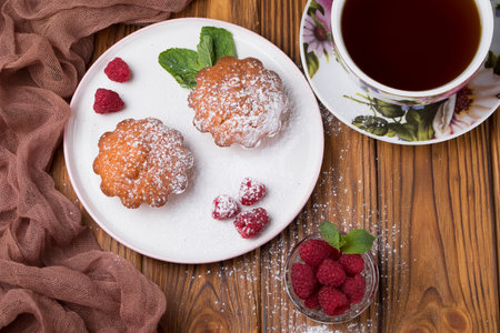 Capcake with raspberries and sugar powder on the table with tea teapot