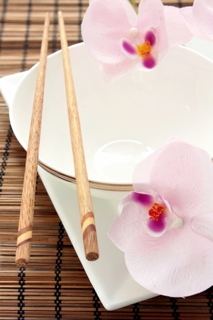 Chinese place setting with a white bowl and plate, chopsticks and orchids.の写真素材