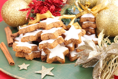 Star-shaped Christmas cinnamon cookies on a green plate. Decorated with gold, red and green Christmas decorations.の写真素材