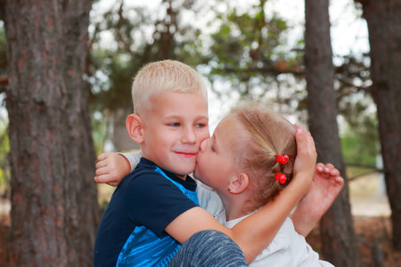 Happy big brother and his cute little sister are in the forest. Fanny girl kissing hugging his...