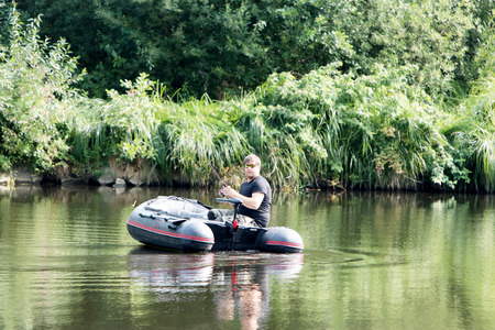 Young man in inflatable boat with electric outboard fishing at river.の写真素材