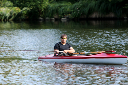 Young man in red kayak paddling by the riverの写真素材