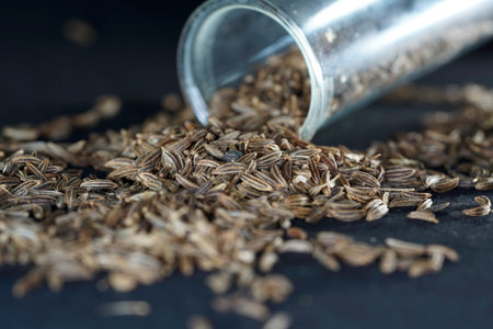Pile of cumin seeds and a glass jar on black backgroundの写真素材