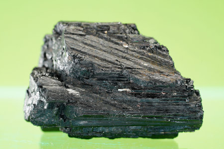Natural mineral from geological collection - piece of black coal on green background