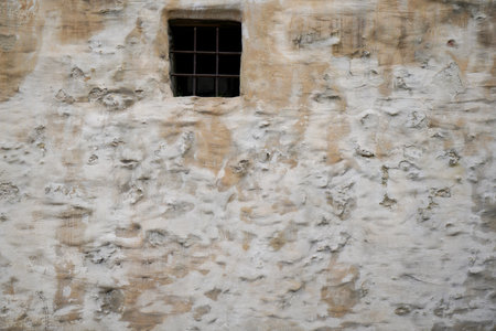 Old stone wall with a window and a grating on it.
