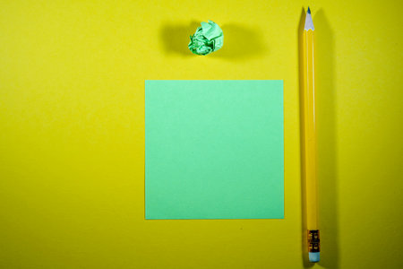 Green paper with pencil and crumpled paper on a yellow backgroundの写真素材