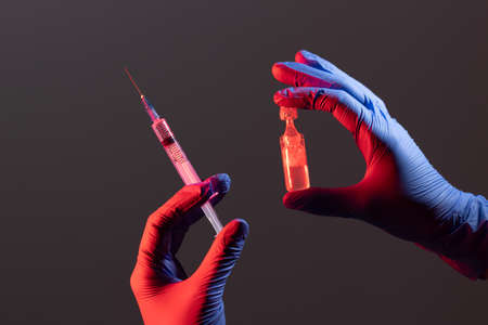 The syringe and the vaccine are held by the hands. Hands in medical gloves. Medical concept.の写真素材