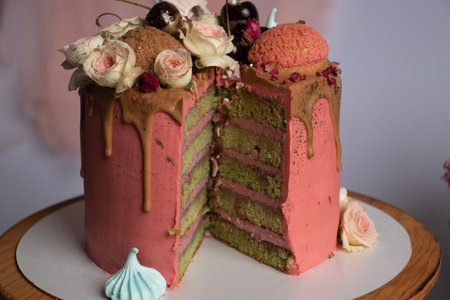 Pink sponge cake with a slice cut off. The cake is beautifully decorated with cookies, meringue and...