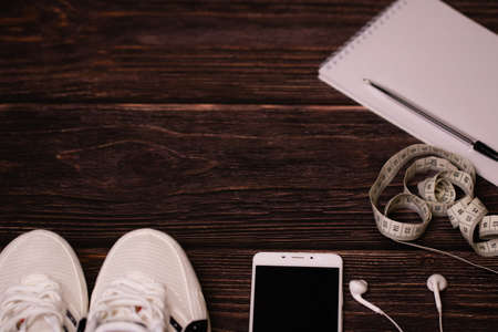 Fitness plan. Planning a workout, sports. On a wooden background, sneakers, headphones, phone, meter, notepad and pen. Space for the text. Top view, flat lay.の写真素材