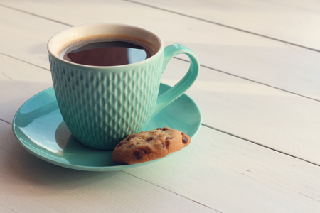 Coffee in a turquoise mug and cookies with chocolate on a white wooden tableの写真素材