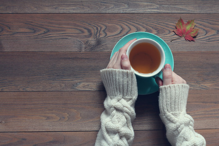 Female hands holding a cup of tea with green tea on a wooden tableの写真素材