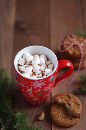 Red Christmas mug of coffee and marshmallows and cookies on the wooden tableの写真素材