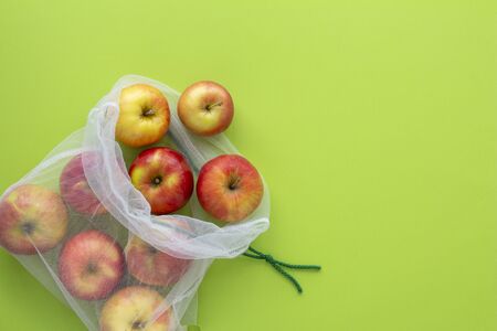 Red apples in eco reusable bag on a green background top view. Eco living conceptの写真素材