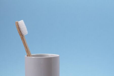 White bamboo toothbrush in white glass on a blue background. Ecological and zero waste conceptの写真素材