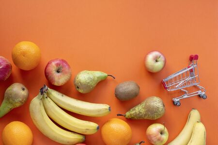 Fruits and small shopping card on a orange background top viewの写真素材