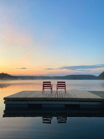 Two red chairs on a wooden pier on a lake at sunrise.の写真素材