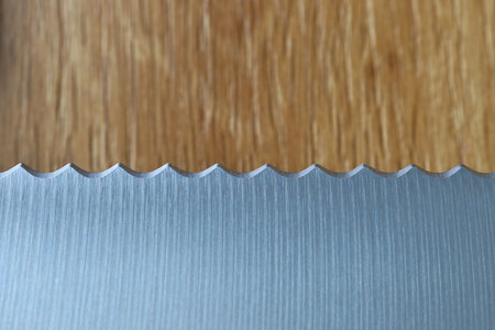 A macro close-up of a serrated stainless steel knife edge against a natural wooden background....