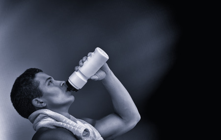 Young muscular man drinking water of bottle after his running or working outdoor. Fitness and healthy lifestyle concept. Isolated on blackの写真素材