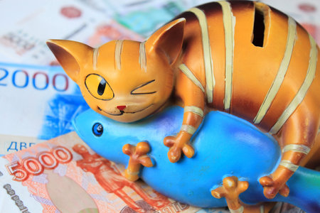 Close-up piggy bank and a lot of money. Moneybox is a cat with a fish.の写真素材