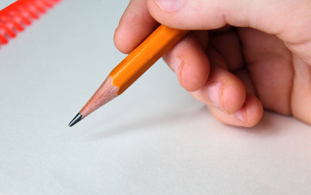 Close-up child hand holding a pencil on sheet of notepad. View of writing and drawingの写真素材
