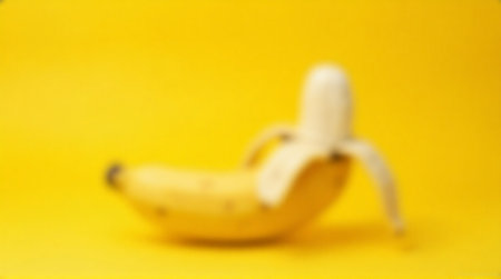 Bright yellow background showcases a partially peeled ripe banana, offering vibrant freshness and healthy energy.の素材
