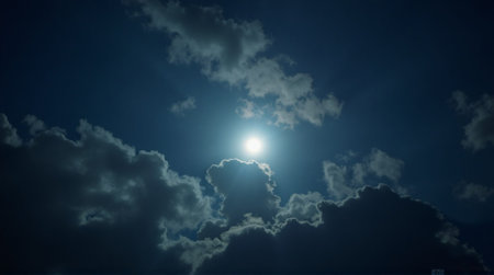 Dramatic sun shining through clouds against deep blue sky for inspirational background imagery and atmospheric designsの素材
