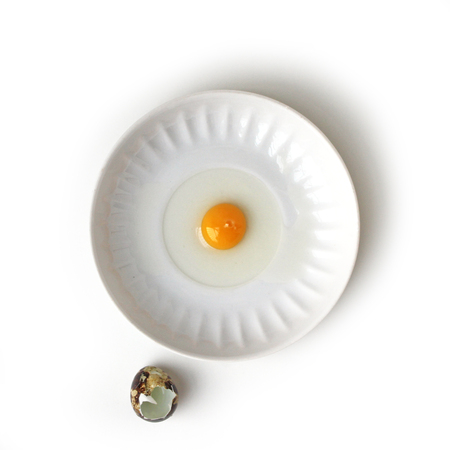 Cracked Quail egg in saucer with eggshell on white background top view, healthy food conceptの写真素材