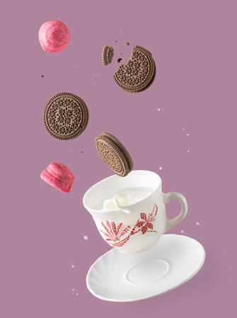 cookies and marshmallows fly over a cup of milk, splashes of milk and cookie crumbs, levitating foodの写真素材