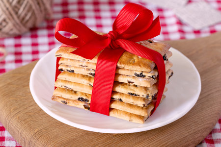 cookies, tied with a red ribbon, are stacked on a white plate. Wooden board and a checkered red towel on the backgroundの写真素材