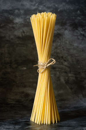 raw spaghetti stands upright on a dark background, tied with a rope. Italian wheat pasta, foodの写真素材