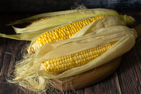 Fresh corn on the cob on a cutting board on a dark wooden background.