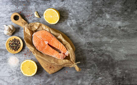 raw salmon fish steak on a dark background. Fish steak in baking paper, lemon, garlic and peppers. Copy spaseの写真素材