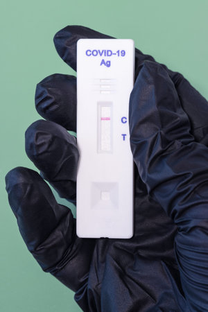 a hand in a black glove holds a negative rapid test for coronavirusの写真素材