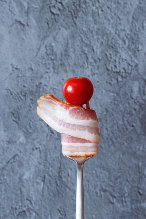 a slice of raw smoked bacon and a cherry tomato on a fork