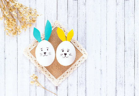 two white eggs with ears and a painted hares face lie on a woven napkin
