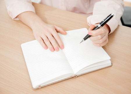 Close up of a woman's hands writing in a notepad placed on a wooden table, home office and work concept, plans and thoughtsの写真素材
