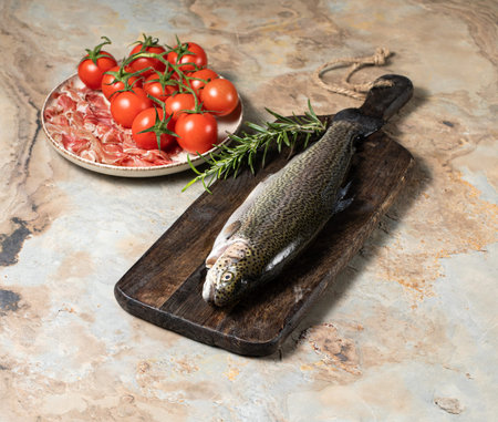 Raw trout with rosemary, prosciutto parma and tomatoes on a wooden vintage background, healthy eating concept, fish. Stock photoの写真素材