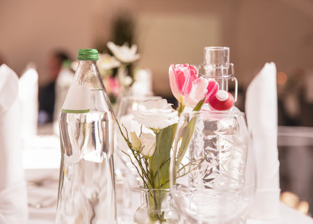 Festive decorated table in a restaurant, wine glasses, vase, flowers, mineral water bottles, textiles, cutlery on a white tablecloth. Restaurant, celebration, weddingの写真素材