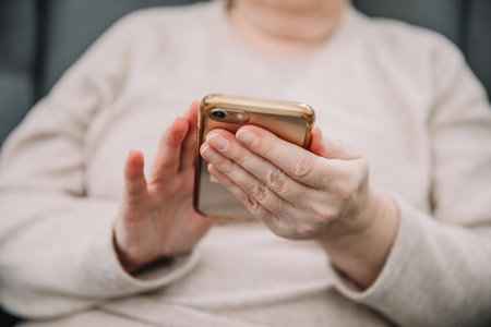 An elderly woman holds and uses a smartphone in her hand, a smartphone. Grandmother hands. Closeup, the concept of family connectionsの写真素材