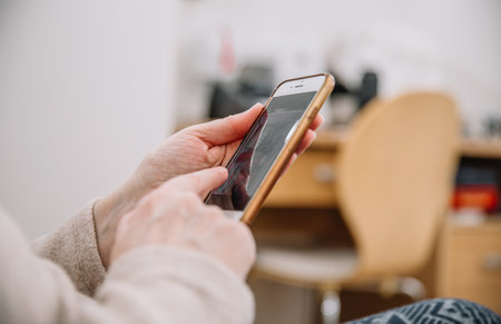 An elderly woman holds and uses a smartphone in her hand, a smartphone. Grandmother hands. Closeup, the concept of family connectionsの写真素材