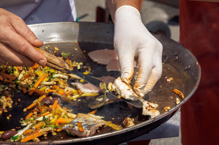 Chef grilling fresh fish, cooking at food festival outdoors, hands in gloves, street food, culinary event conceptの写真素材