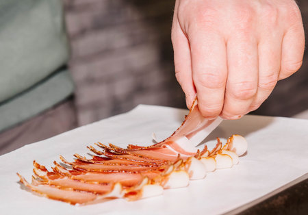 Chef arranging thin slices of cured ham, preparing prosciutto delicately on white paper, presenting gourmet meat, fine cooking conceptの写真素材