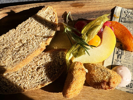 Rustic bread with fried croquettes, fruit, and herbs on wooden board.の写真素材