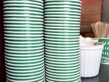 Stacked green and white paper cups with coffee stirrers in a cafe setting.の写真素材