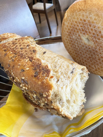 Rustic bread duo on table: seeded baguette and round loaf in dining setting.