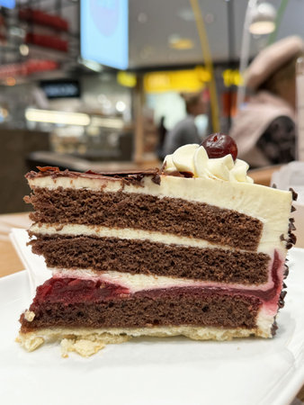 Delicious slice of black forest cake with chocolate, cream, and cherry topping in cafe setting.