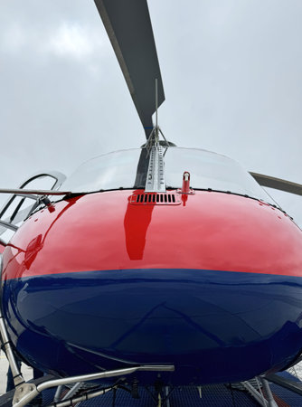 Red and blue helicopter close-up with rotor blades against cloudy sky.の写真素材