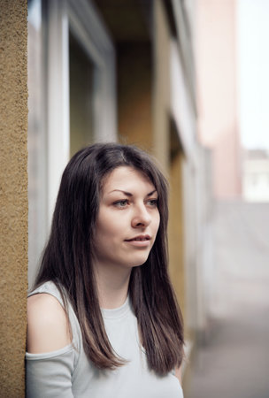 A young woman looking to the side while standing near a beige wall in a calm urban settingの写真素材